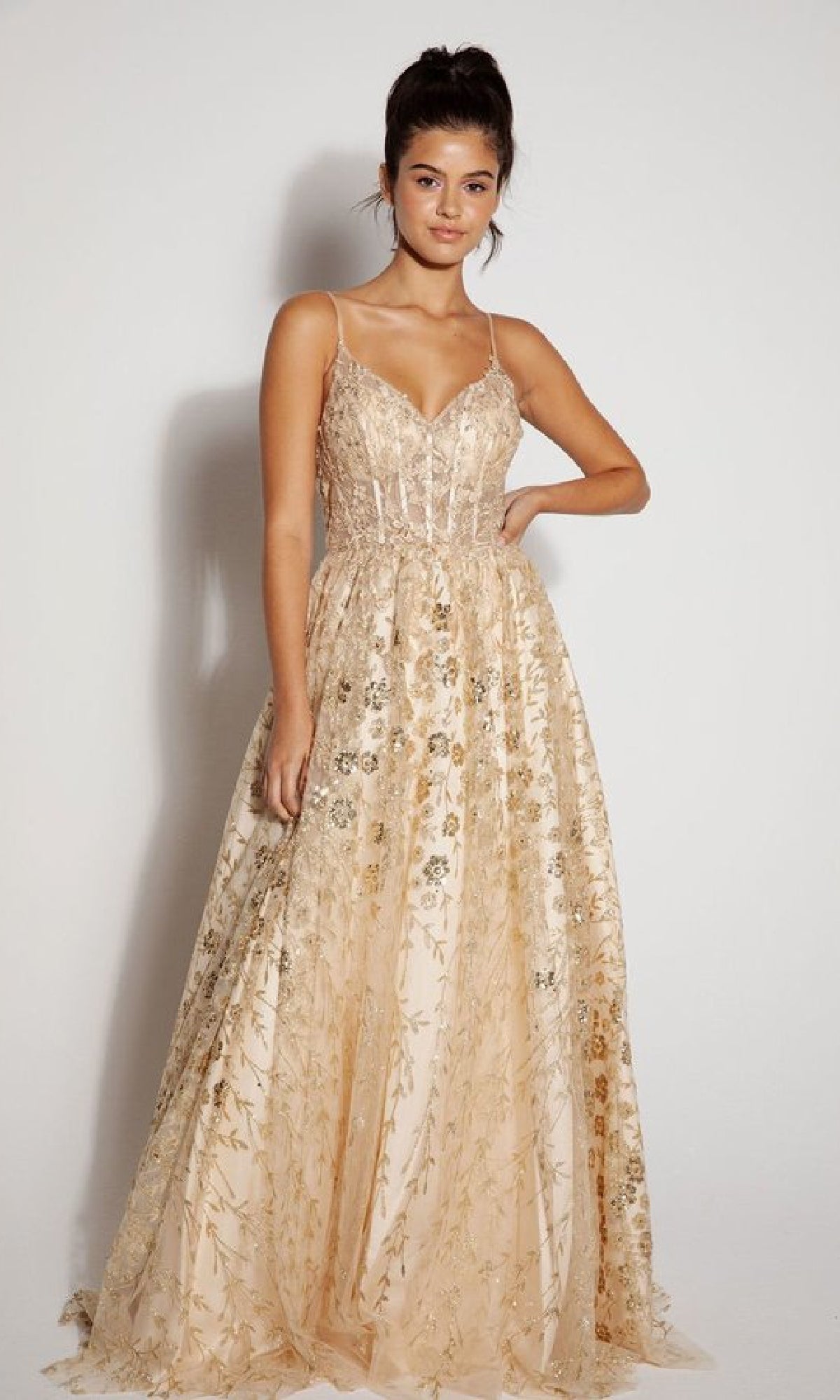 A woman stands against a plain background wearing the Eureka 9908 Long Glitter A-Line Prom Dress—a floor-length, sleeveless formal gown with thin straps and a gold floral print.